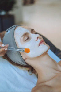 White facial mask being gently applied with a brush during a sculptural facial treatment session.